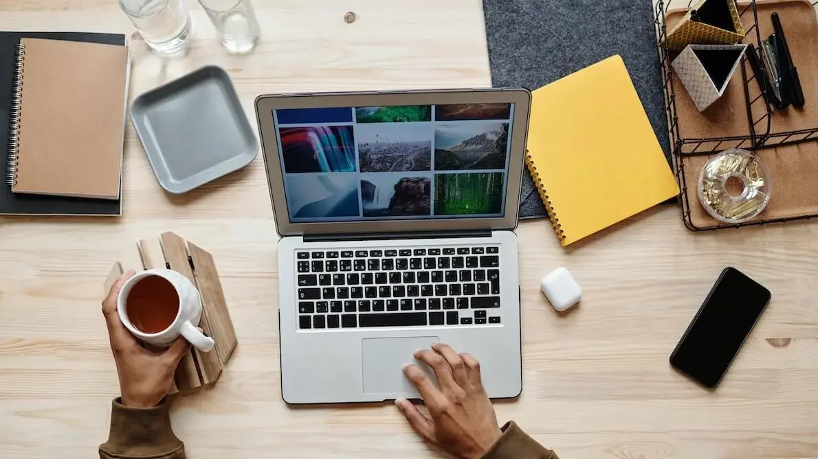 Top view of a person working on a laptop at a wooden desk, holding a cup of tea